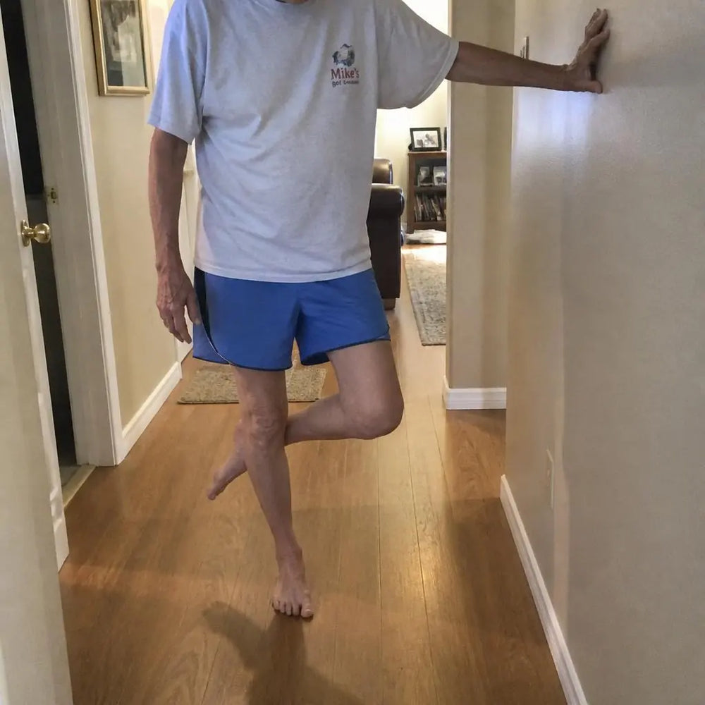 Thin lower legs of an older adult balancing on one foot near a wall for support